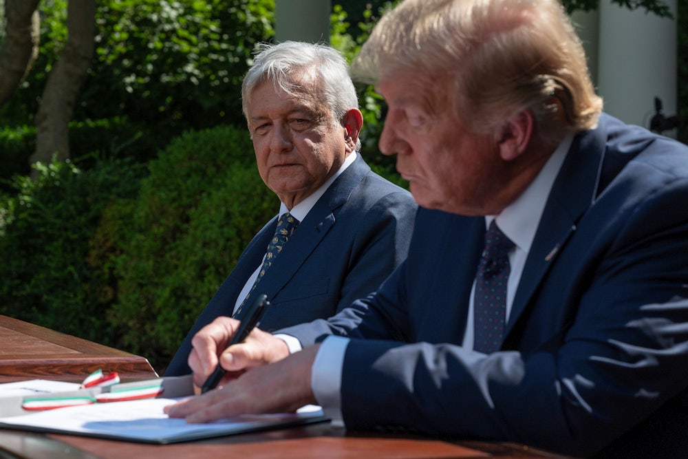 President López Obrador looks at President Trump, both seated at a desk as Trump signs a document.