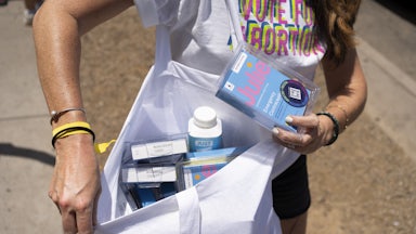 A person shows the contents of a bag full of emergency contraception while wearing a shirt that reads "Vote for Abortion"