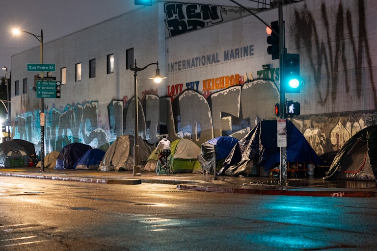 Multiple tents line the sidewalk, as one person bikes by.