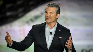 Defense Secretary Pete Hegseth gestures and makes a winking face while speaking at a podium