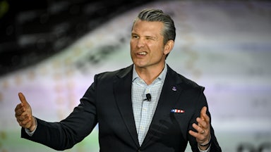 Defense Secretary Pete Hegseth gestures and makes a winking face while speaking at a podium