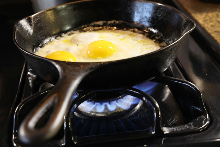 Two eggs fry in a cast-iron pan on a gas burner.