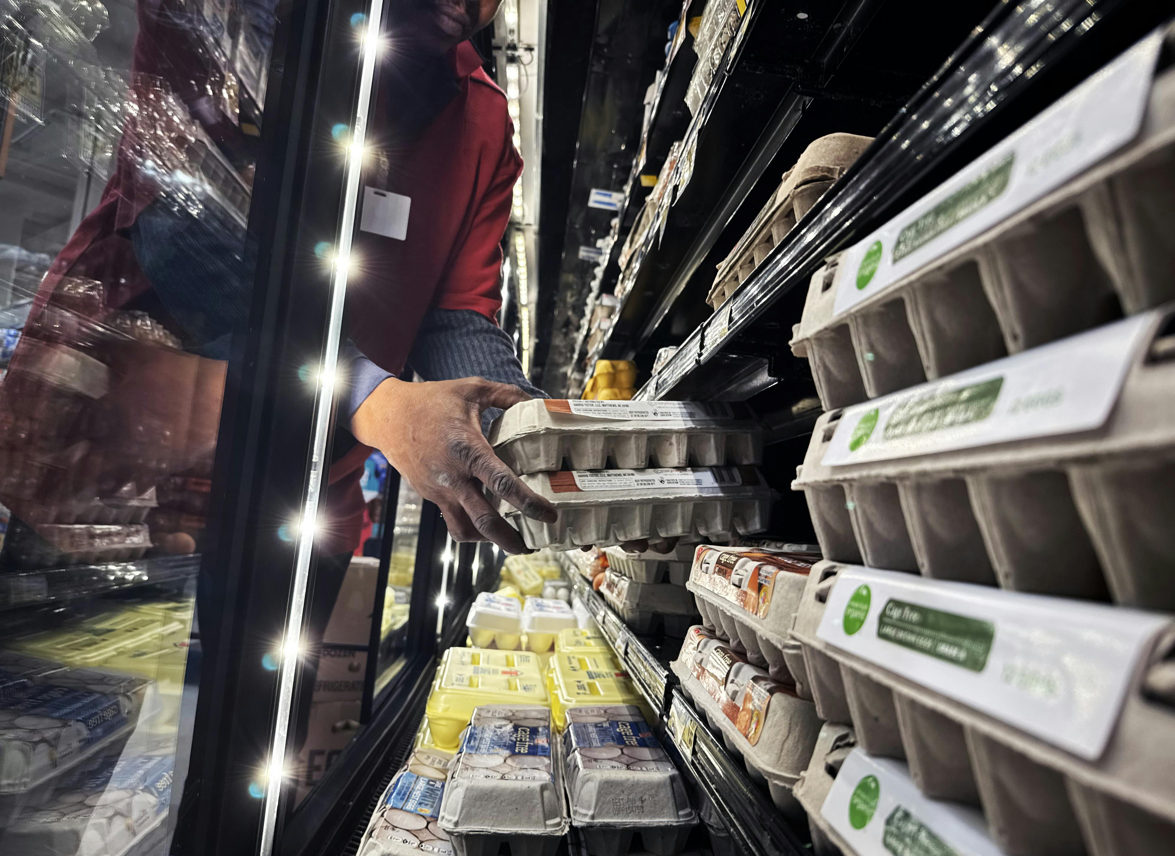 Hands reach into a display case holding cartons of eggs.
