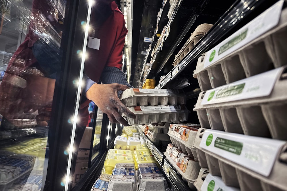 Hands reach into a display case holding cartons of eggs.