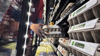 Hands reach into a display case holding cartons of eggs.