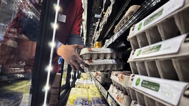 Hands reach into a display case holding cartons of eggs.