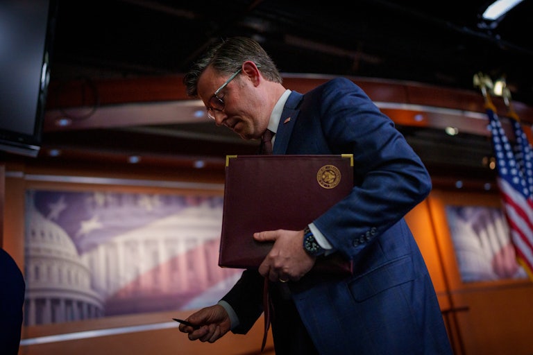 Mike Johnson holds a folder in his arm and looks down while walking out of a press conference