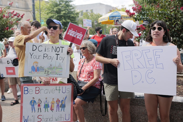 People hold up signs at a protest against the National Guard’s presence in Washington, D.C.