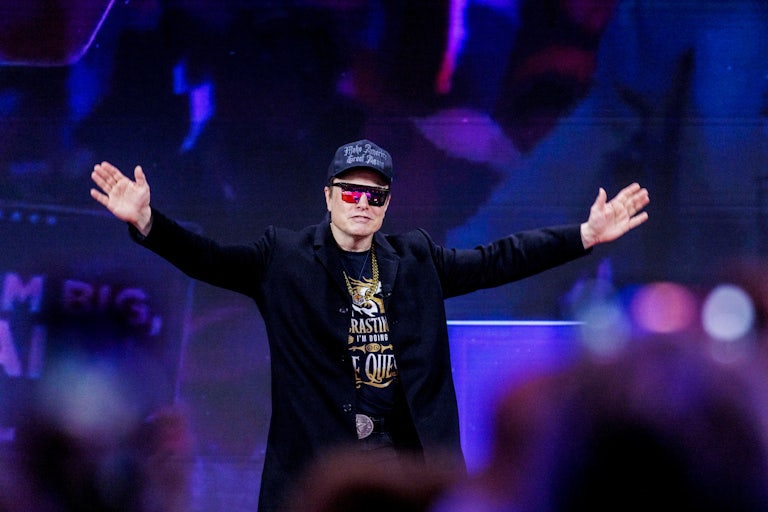 Elon Musk holds his arms out while on stage at CPAC