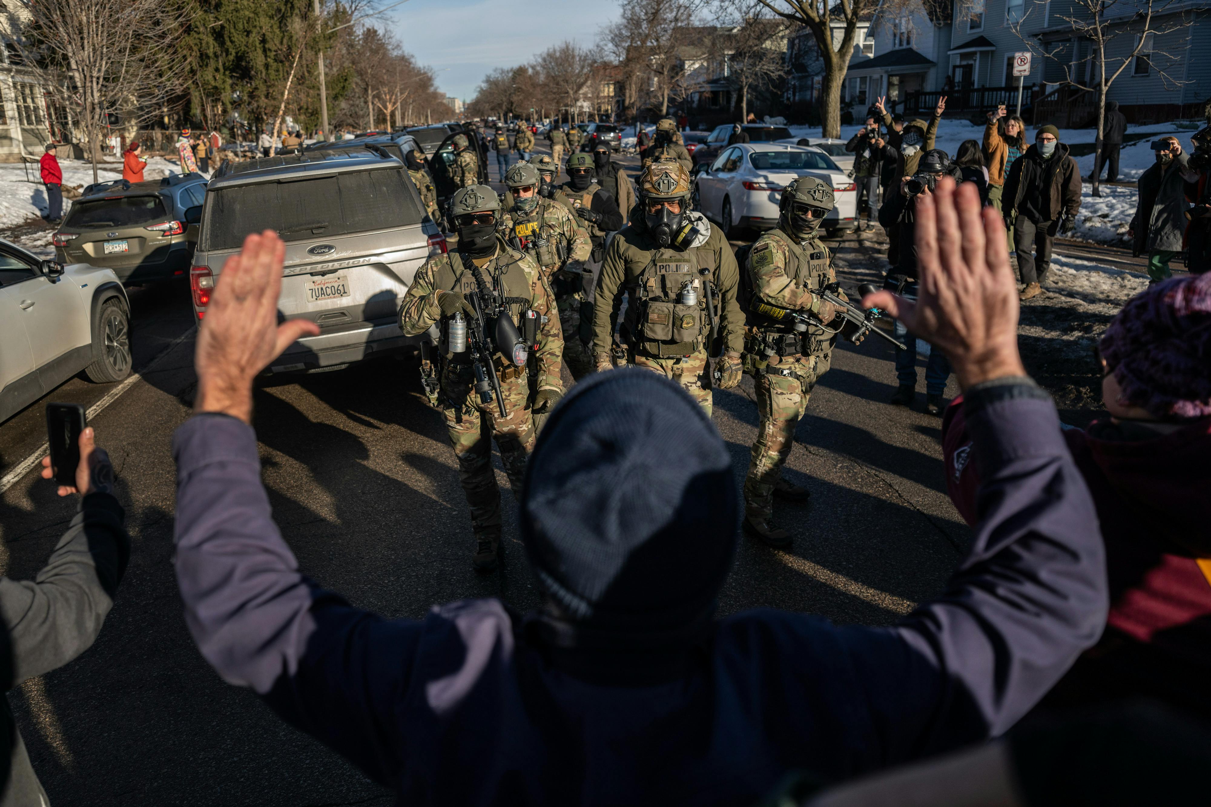 A protester stand with their hands raised above their head as masked federal immigration agents walk towards them