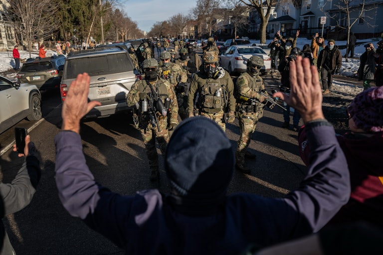 A protester stand with their hands raised above their head as masked federal immigration agents walk towards them