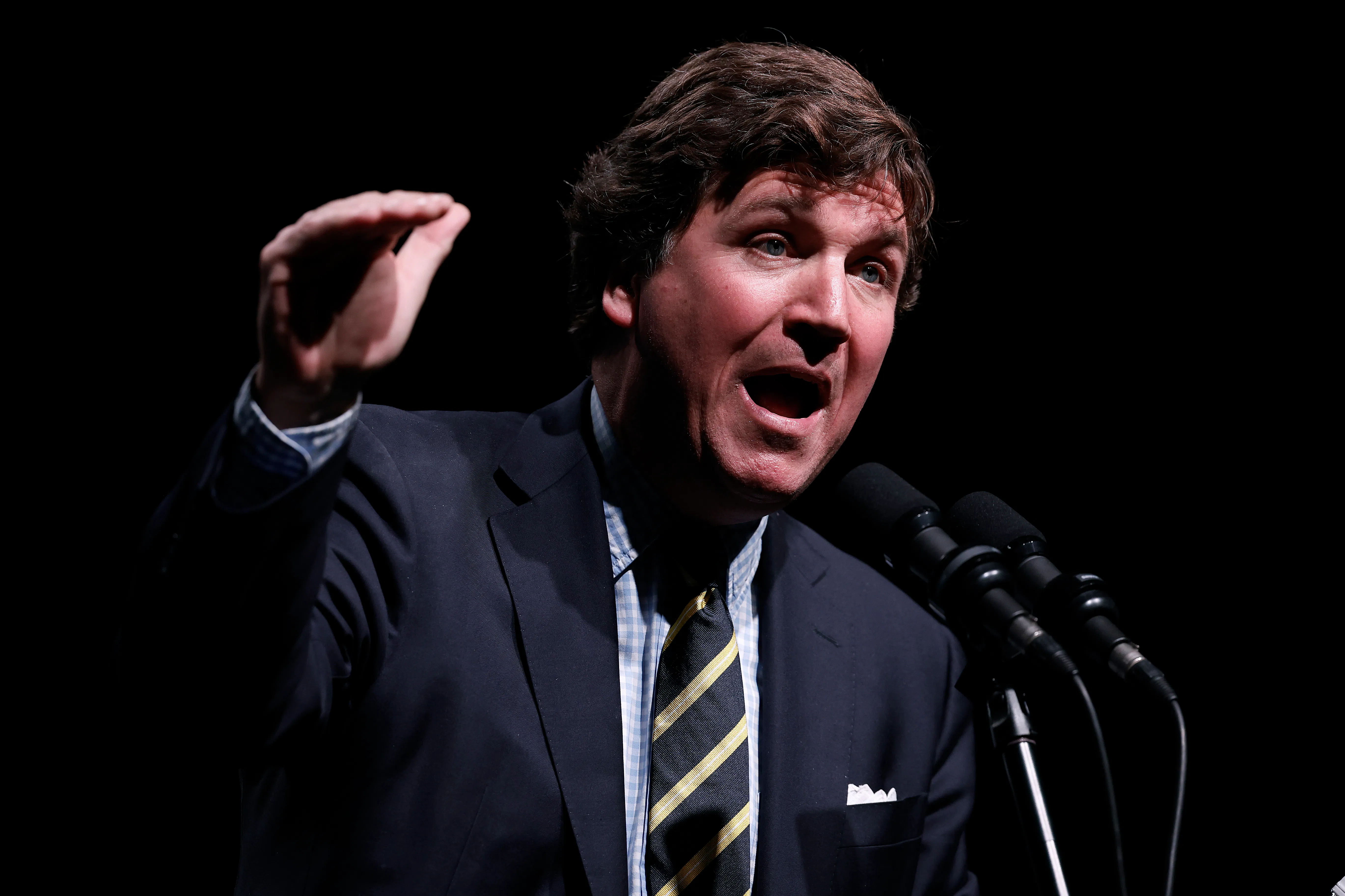 Tucker Carlson gestures and speaks at a podium