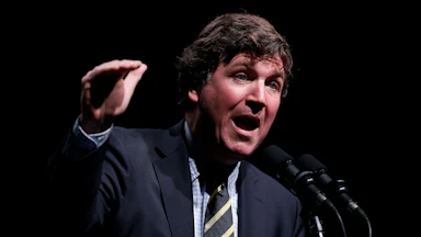 Tucker Carlson gestures and speaks at a podium