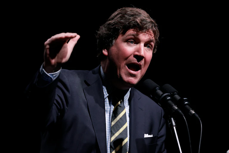 Tucker Carlson gestures and speaks at a podium