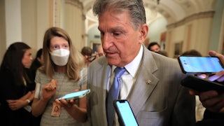 Joe Machin walks through the halls of Capitol Hill surrounded by reporters with mobile phones.