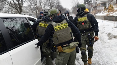 Three ICE agents in the snow open the doors to a white SUV