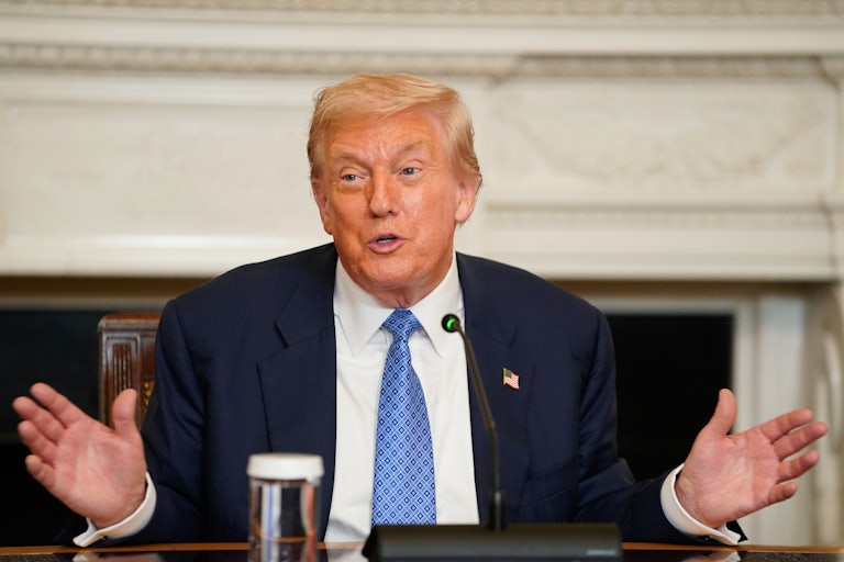 Donald Trump holds his hands out to the side while speaking. He is sitting at a dining table in the White House.