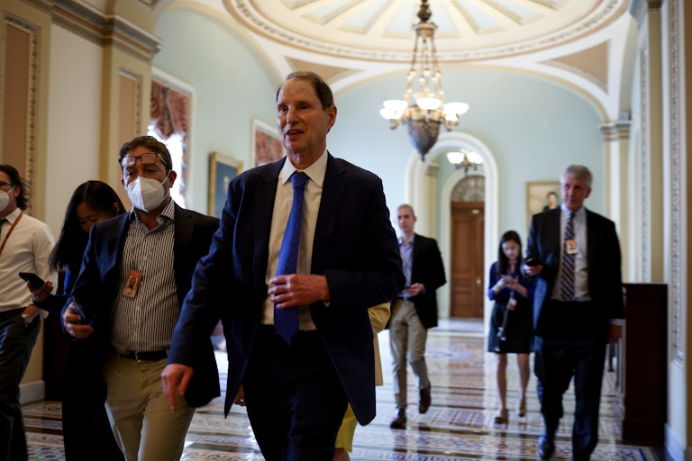 Oregon Senator Ron Wyden, wearing a blue suit and tie, walks past the Senate chambers. 