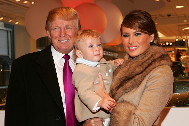 Donald Trump and Melania Trump smile as she holds a baby Barron in her arms.