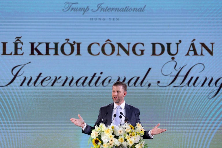 Eric Trump makes a speech in front of a lectern with flowers. Behind him is a large sign that reads Trump International, Hung Yen.