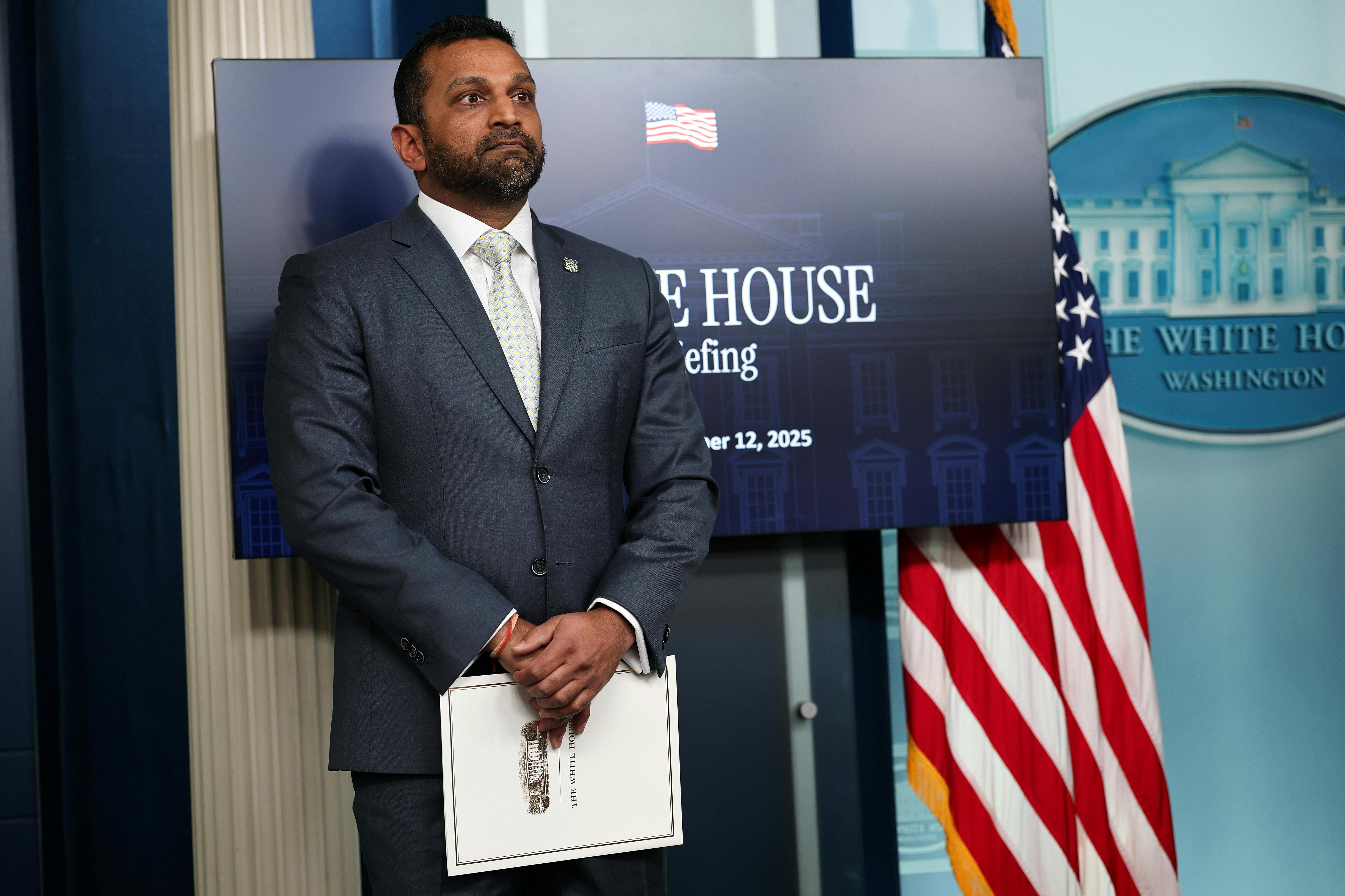 FBI Director Kash Patel stands in front of a screen in the White House press briefing room with his hands folded in front of himself