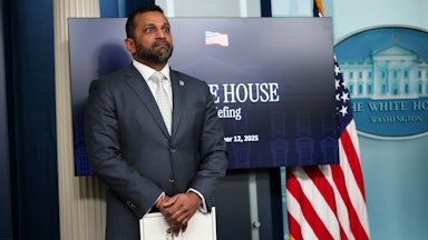 FBI Director Kash Patel stands in front of a screen in the White House press briefing room with his hands folded in front of himself