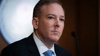 Lee Zeldin is seen wearing a dark suit and light blue tie.