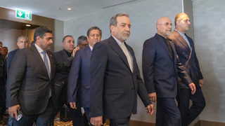 Several Iranian officials wearing suits walk on carpet through a hallway in Switzerland.