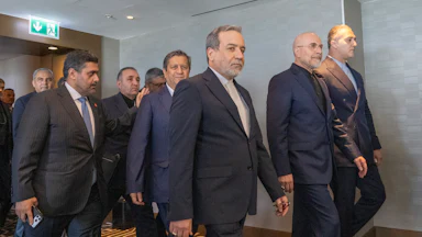 Several Iranian officials wearing suits walk on carpet through a hallway in Switzerland.