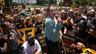 Alexandria Ocasio-Cortez holds a microphone, surrounded by activists.