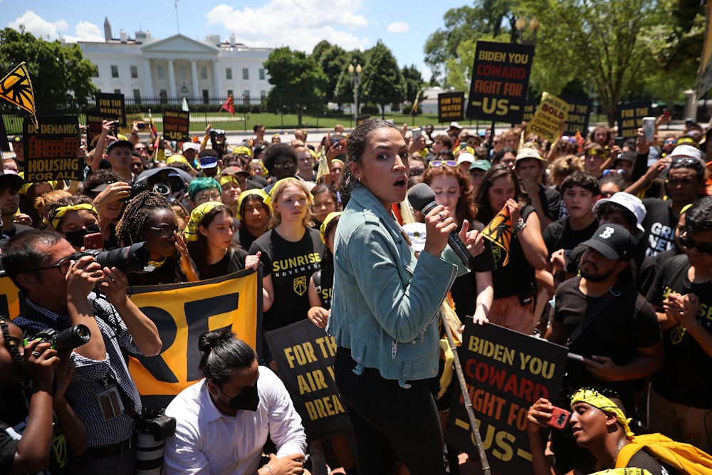 Alexandria Ocasio-Cortez holds a microphone, surrounded by activists.