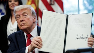 Donald Trump holds up a signed executive order while seated at his desk in the White House.