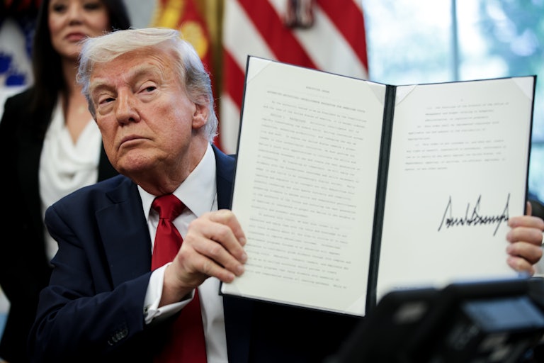 Donald Trump holds up a signed executive order while seated at his desk in the White House.