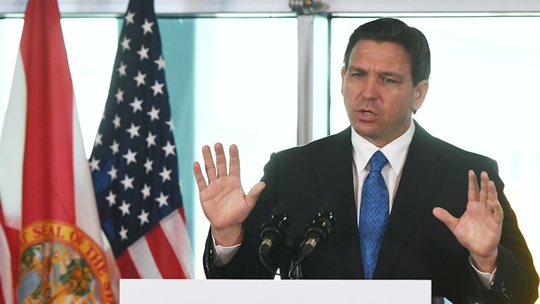 Ron DeSantis holds his hands up while speaking.