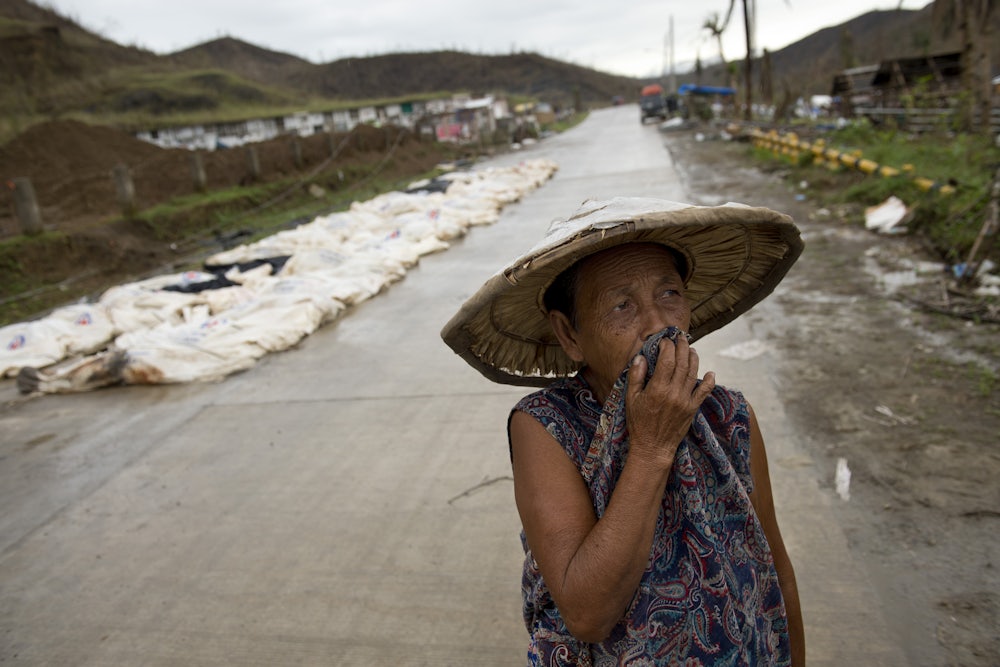 A woman walks past the bodies of Typhoon Haiyan victims awaiting burial in a mass grave in the Philippines.