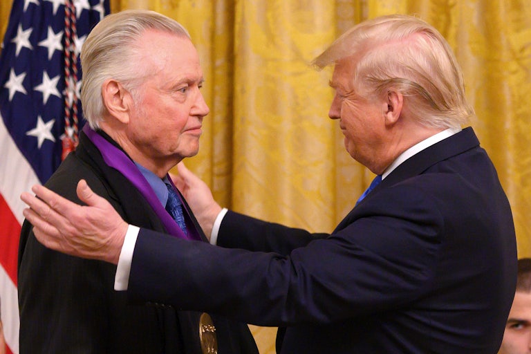 Donald Trump puts both hands on Jon Voight's shoulders after placing the medal around his neck