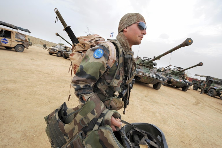 A French soldier clad in fatigues bearing the European Union's regalia carries his gear back to camp.