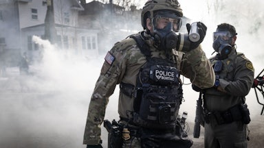 Two Border Patrol agents wear gas masks as tear gas is in the air.