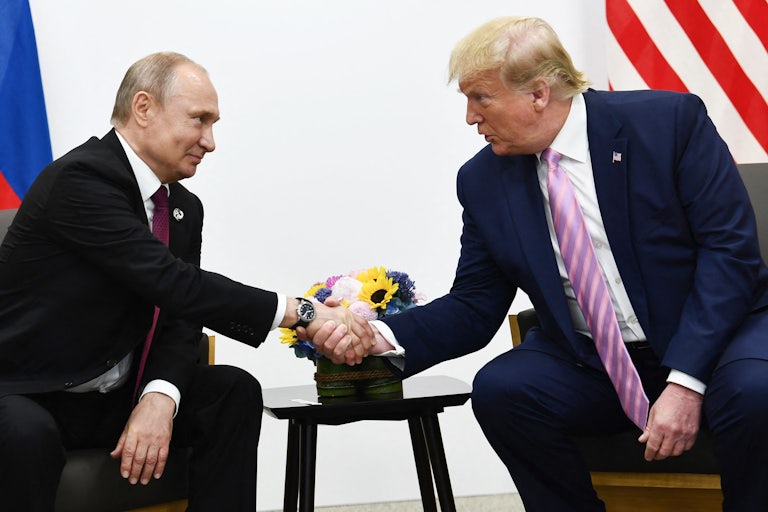 Russian President Vladimir Putin and Donald Trump, both seated, reach over and shake hands, looking into each other's eyes.