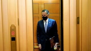 A masked Mitt Romney stands alone in an elevator.