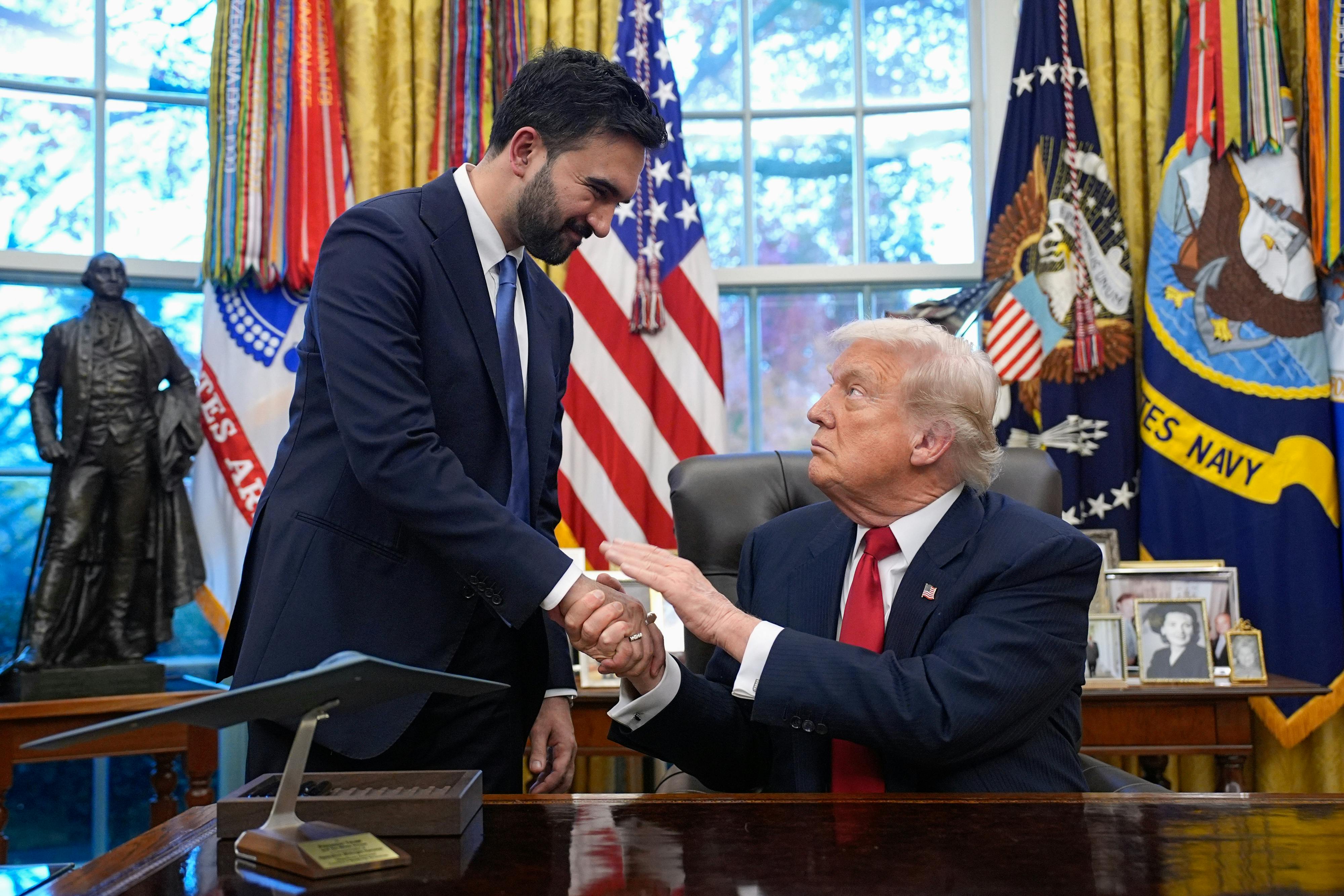 Zohran Mamdani and Donald Trump shake hands. Trump is sitting at his desk in the Oval Office