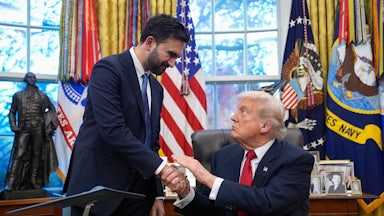 Zohran Mamdani and Donald Trump shake hands. Trump is sitting at his desk in the Oval Office
