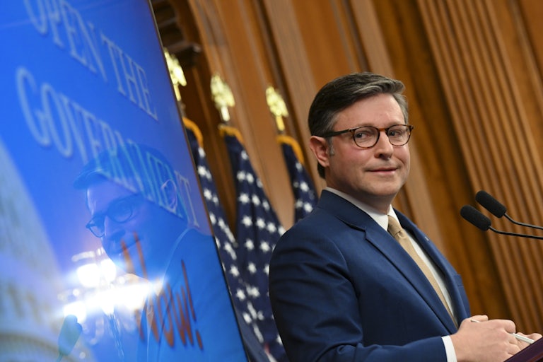 House Speaker Mike Johnson looks to the side and makes a weird face while standing at a podium