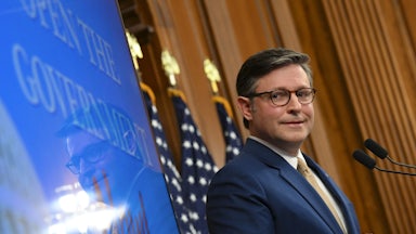 House Speaker Mike Johnson looks to the side and makes a weird face while standing at a podium