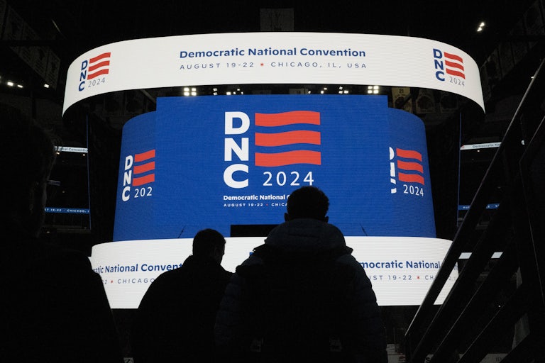 Two silhouettes in front of a large screen that reads "DNC 2024" and "Democratic Natioanl Convention"