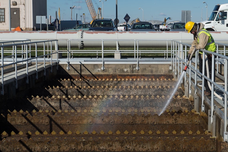 A worker sprays water into a wastewater tank.