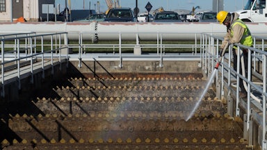 A worker sprays water into a wastewater tank.