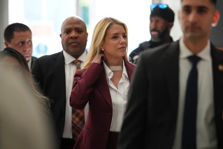 Pam Bondi brushes her hair over her shoulder and smiles while walking in a crowd of people