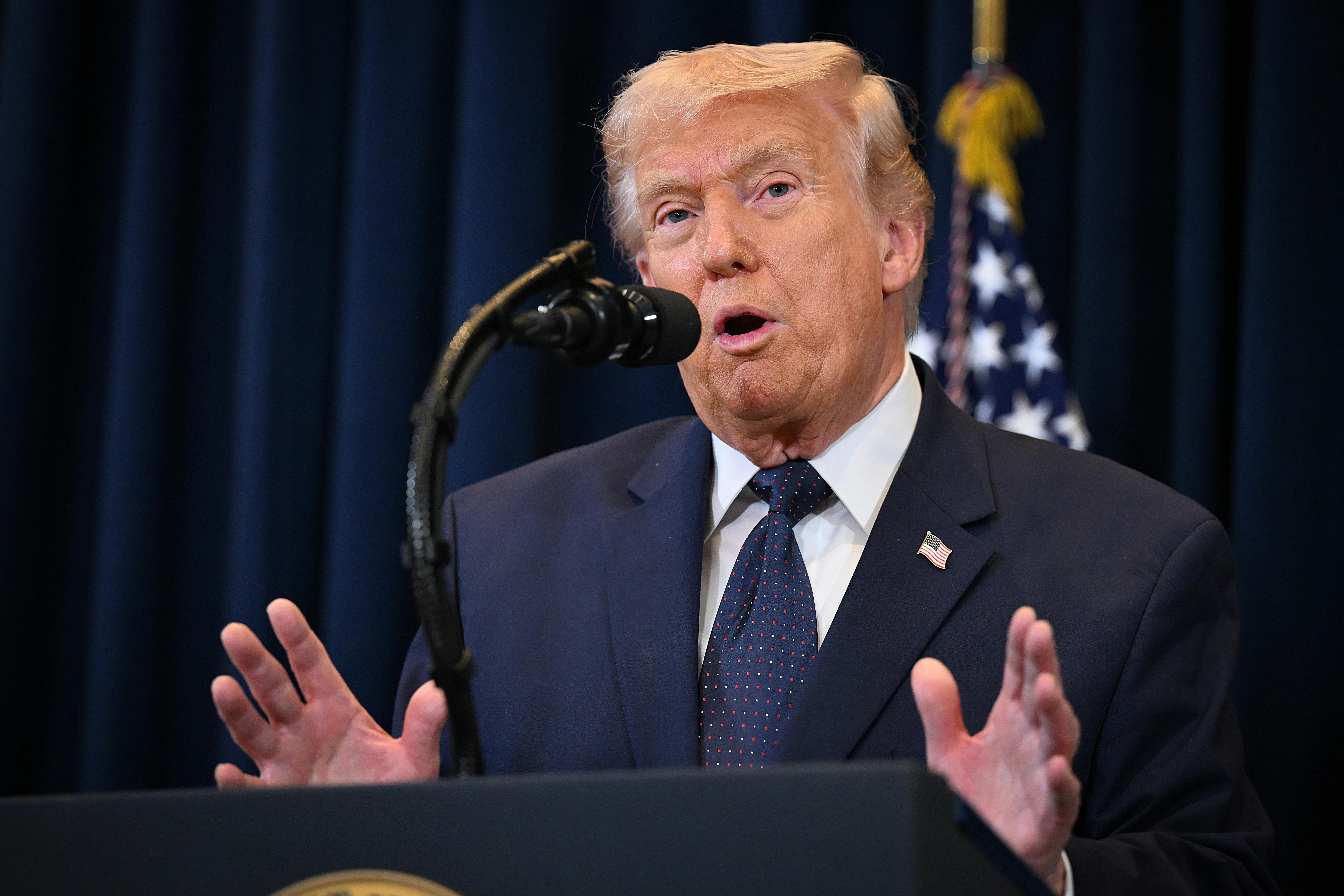 Donald Trump gestures with both hands while speaking at a podium