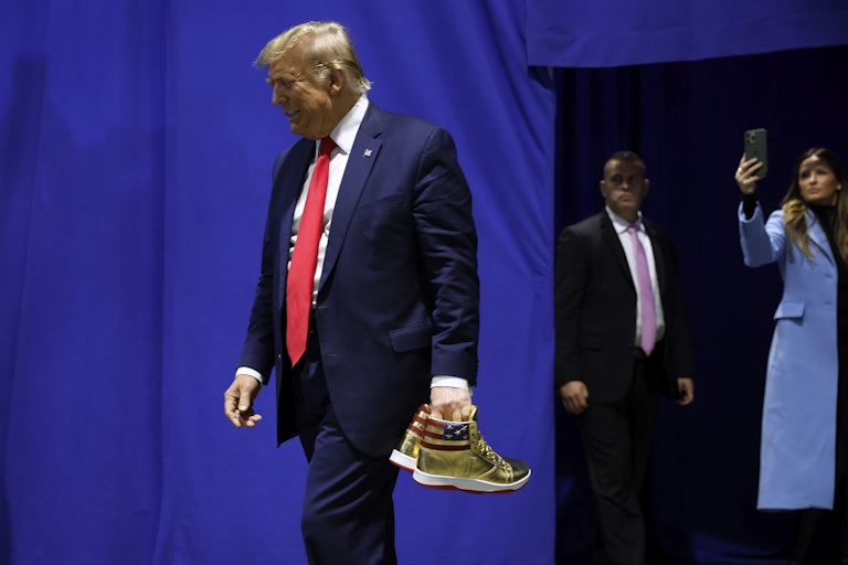 Donald Trump walks, head faced down, as he carried a pair of gold sneakers (emblazoned with the US flag) in his left hand